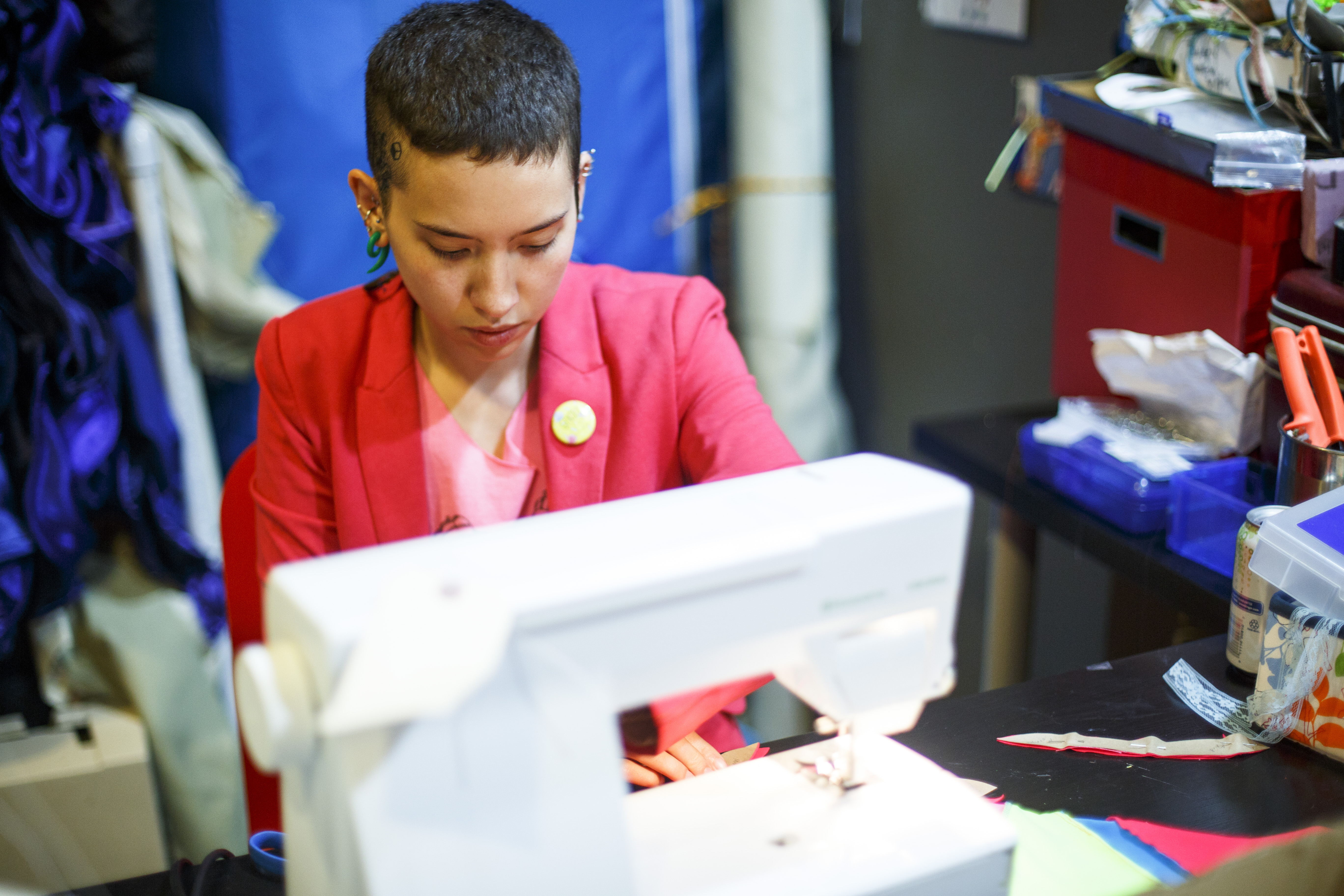 Sky Cubacub sits at their sewing machine, while wearing a pink blazer. Their studio, located within their home, is essential to their process and practice. Photo credit Grace DuVal.