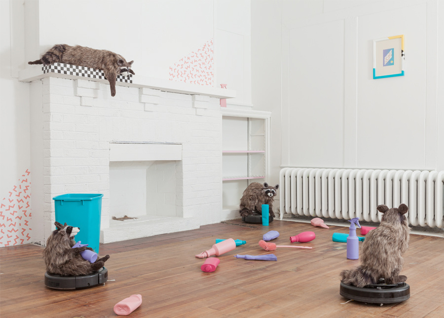 Three homemade raccoons balanced on top of Roombas in a room scattered with multicolored bottles of cleaning products. In the background, a fourth raccoon is balanced on top of a white fireplace, and seems to look down on the scene. Lux, Maria. “Dominus.” 2017. installation view. “Dominus,” DEMO Project, Springfield, IL. Courtesy of artist. Photos: Will Arnold.