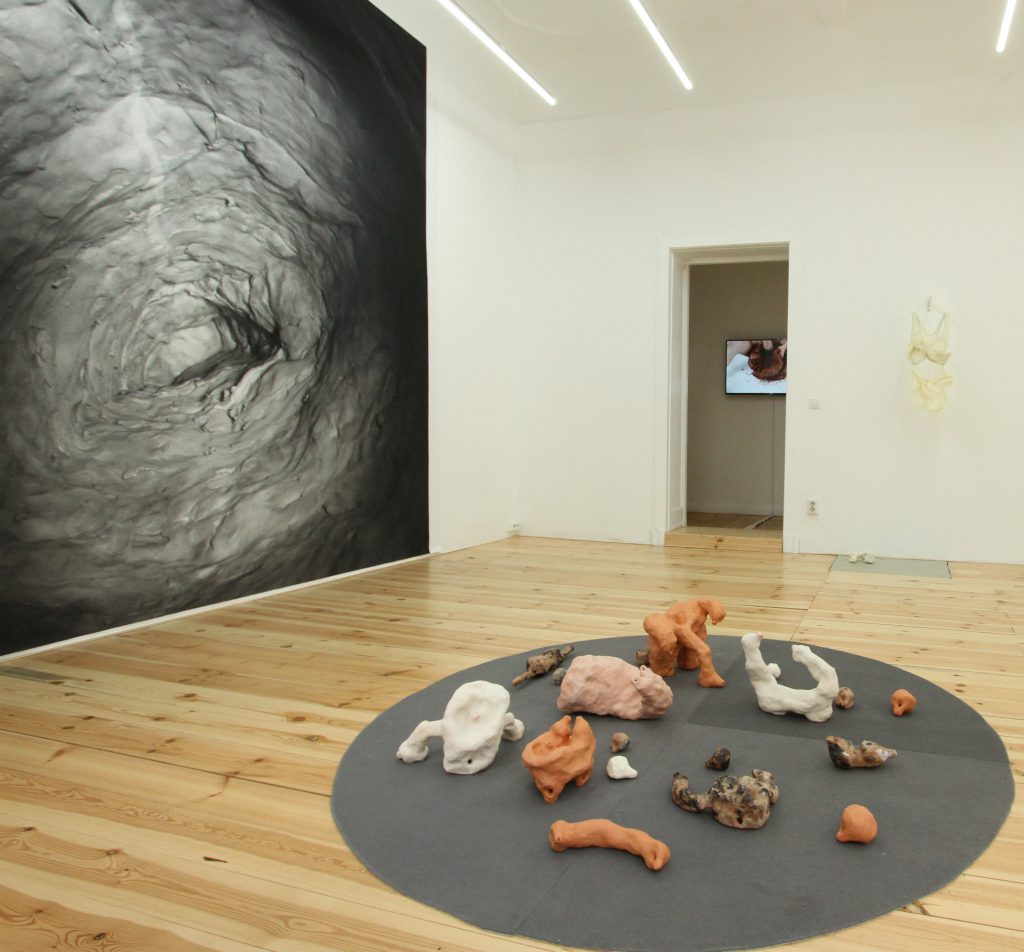 Photo courtesy of artist. Image features a gallery space with a large image on the left side on the wall and a series of sculptural pieces on the floor. 