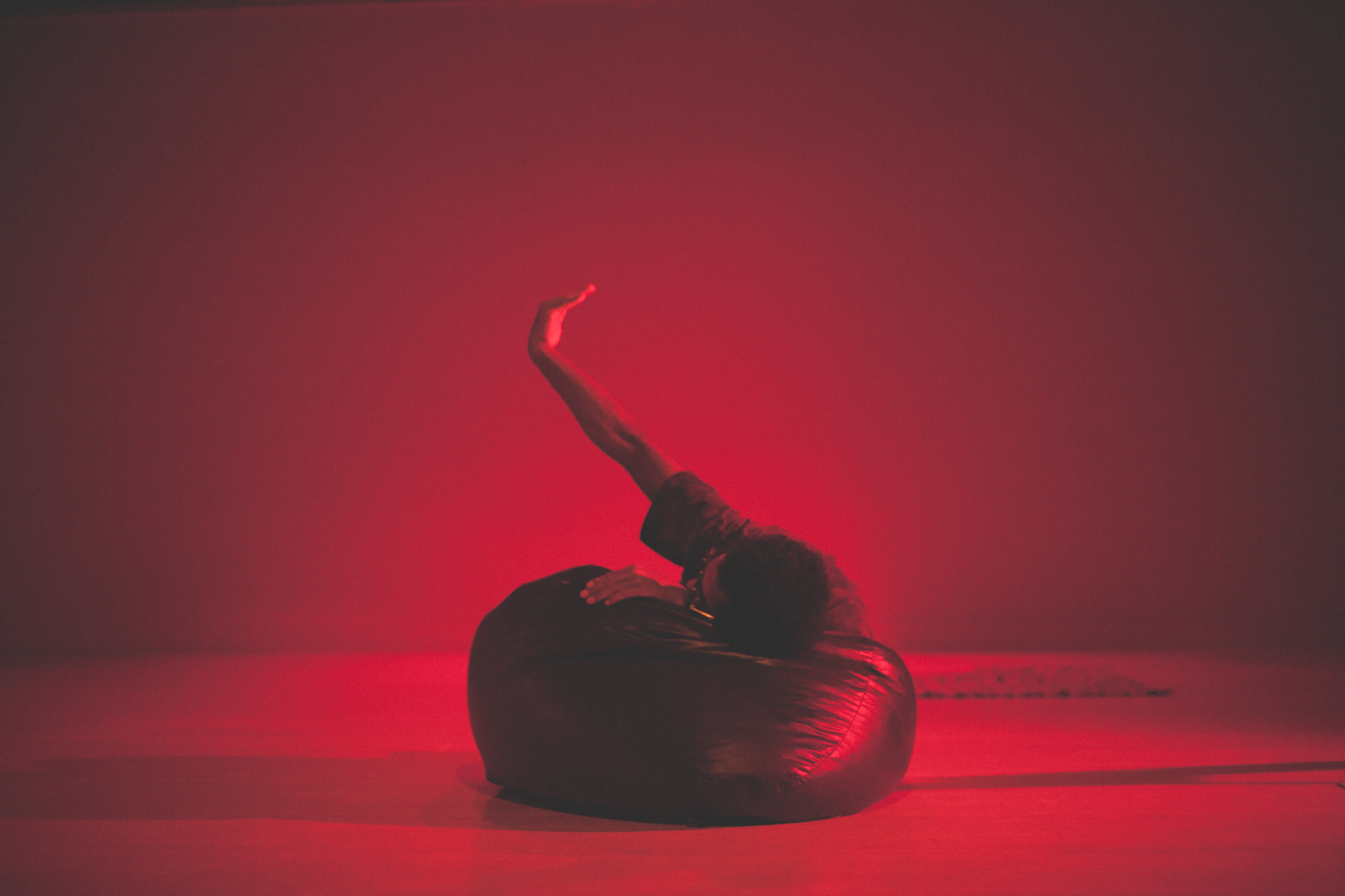 Swathed in red light, Joelle Mercedes performs at Links Hall. Mercedes leans on a cushion with one arm in the air. Photo by Ally Almore