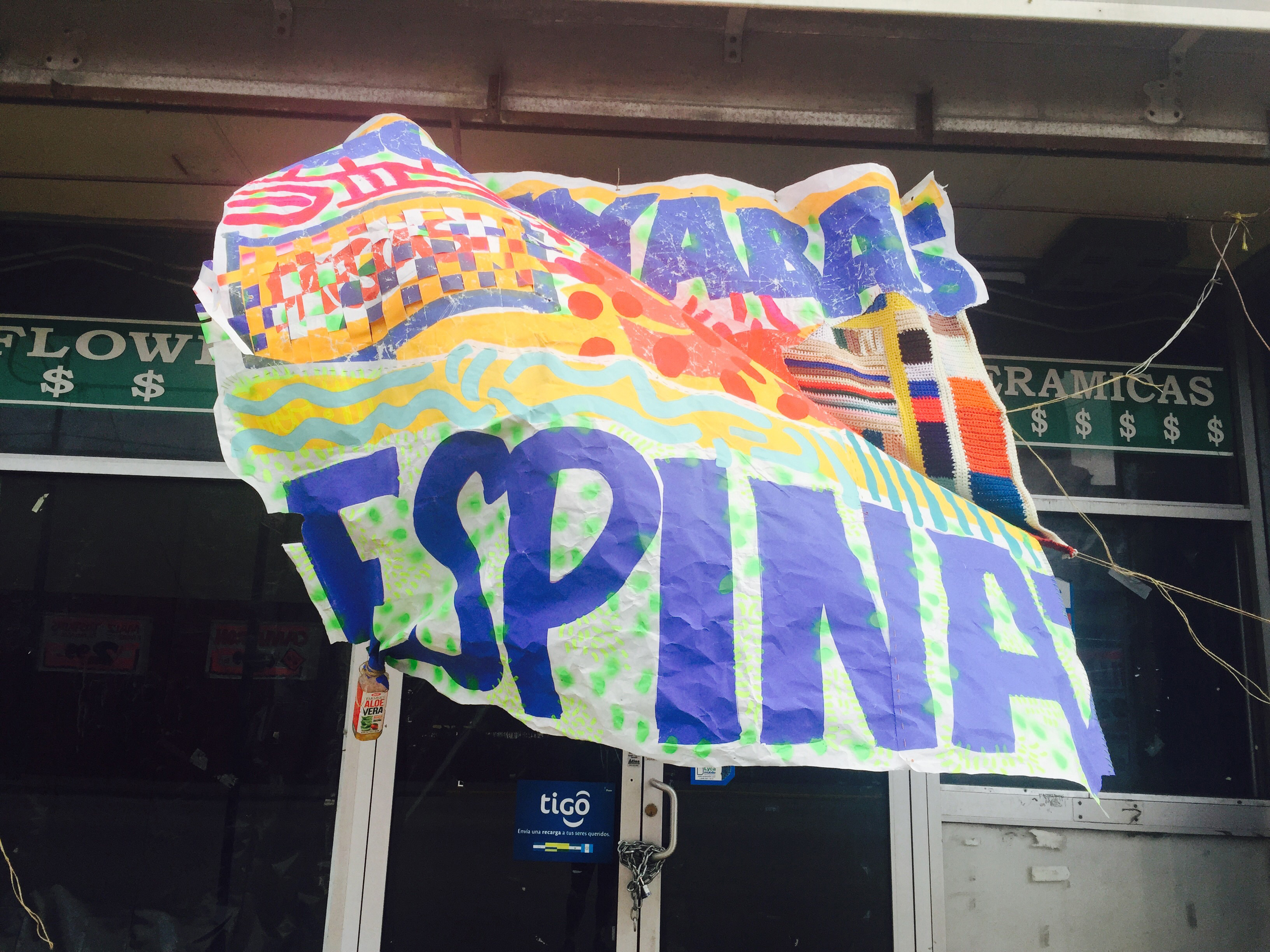 “Guayaba spine memory blanket,” 2017. Collaged and woven hand-made grocery signs stitched together and painted over with colorful patterns in select areas. A knitted textile of colorful stripes and bands is stitched on the right side. The work is installed outside of a storefront in Pilsen. 