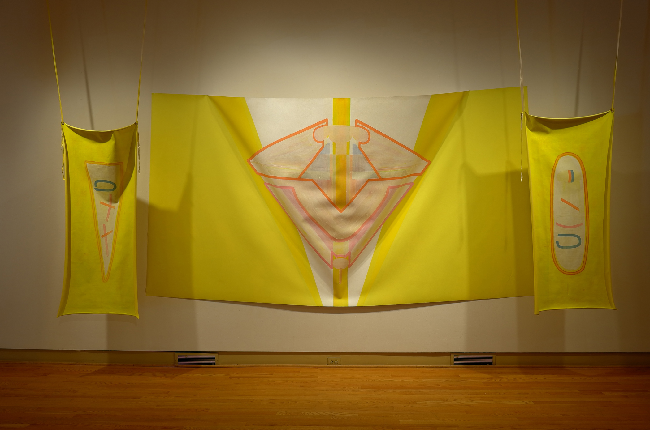 Roni Packer, Trying to Paint G-d, 2018. Oil and latex paint on canvas, 136 x 70 inches (center) and 25 x 60 inches (left and right). Packer’s primarily yellow and pink flag-like canvas slumps softly from the wall while flanked by two hanging banners containing pink and blue semi-geometric markings. Photo courtesy of the Ukrainian Institute of Modern Art.