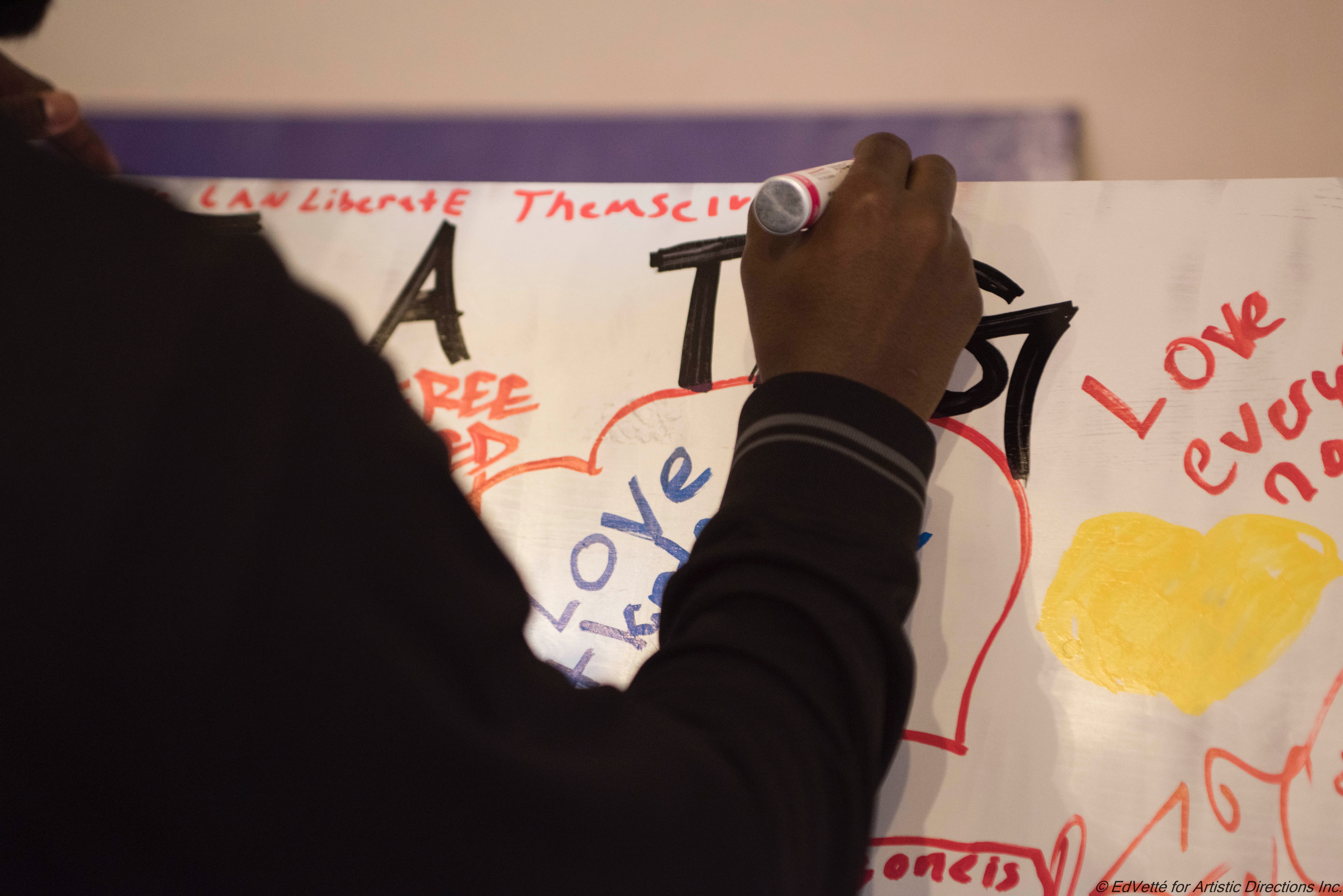 A hand is positioned atop a white canvas while filling in text on community canvas during culminating event for first session of Envisioning Justice at Circles and Ciphers.