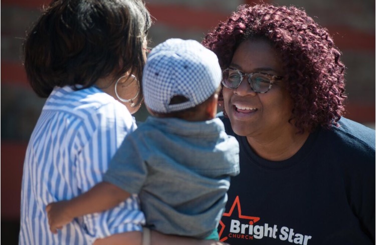 Image: A member of Bright Star Community Outreach speaks with a person holding a child