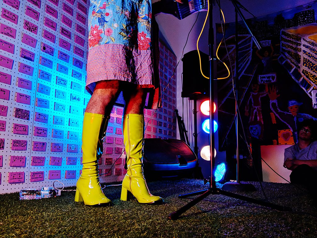 Image: Alok's lime green, patent leather gogo boots stand out on astroturf covered stage. Photo by Chelsea Ross.