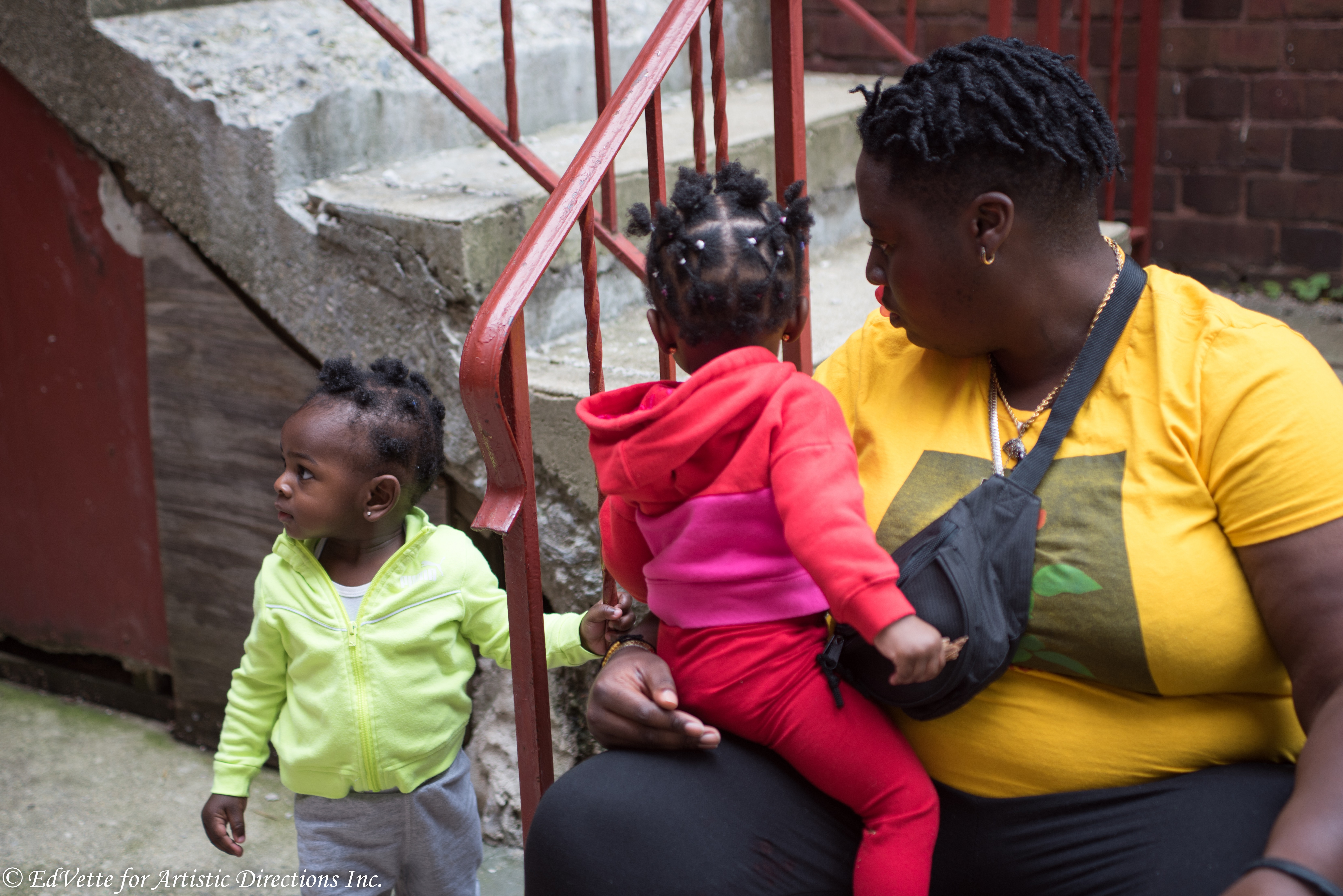 IMAGE: AnnMarie Brown sits on a stairwell outside of United Church of Rogers Park with a child seated on her lap and another standing a short distance away.