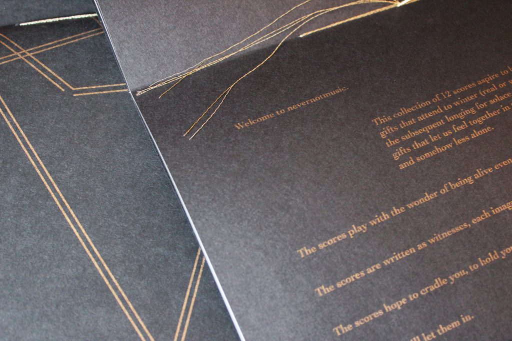 Image: Udita Upadhyaya’s book “nevernotmusic” (detail). The book lies open to the centerfold, showing black paper, gold thread, and gold type. Part of the lower page is visible, with the text beginning, “Welcome to nevernotmusic,” and including part of a description of the project of 12 scores and phrases like “The scores play with the wonder of being alive even…” and “The scores are written as witnesses….” Behind the open centerfold is part of the front cover of another copy. Photo by Caleb Neubauer.