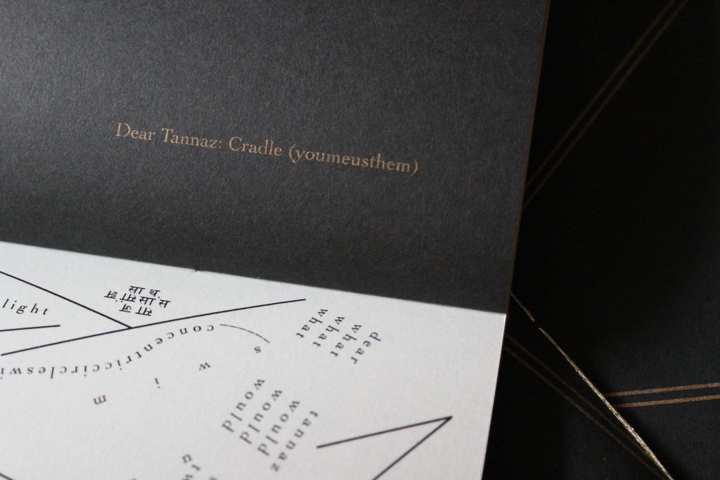 Image: Udita Upadhyaya’s book “nevernotmusic” (detail), showing part of the score, “Dear Tannaz: Cradle (youmeusthem).” Part of one page-spread is visible, with opaque black paper on the upper page (where the score’s title appears in gold type) and with whitish vellum on the lower page (with lines, open triangles, and straight and curved lines of text in English and Hindi, printed in black ink). In the background, beyond this copy, is part of the front cover of two other copies, with gold stitching and straight gold lines on black paper. Photo by Caleb Neubauer.