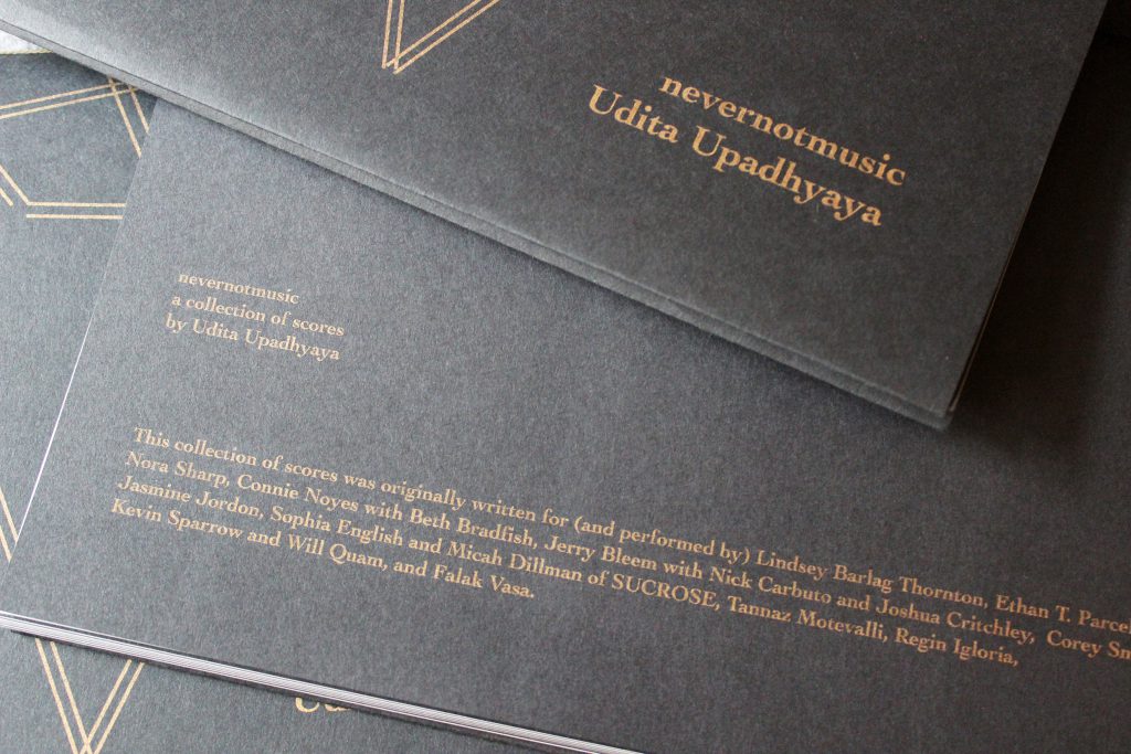 Image: Udita Upadhyaya’s book “nevernotmusic” (detail). Three copies are in a loose pile, showing parts of the front cover and of the back cover (beginning with “nevernotmusic / a collection of scores / by Udita Upadhyaya” and listing the performers for whom the scores were originally written). Text and motifs are in gold on black paper. Photo by Caleb Neubauer.