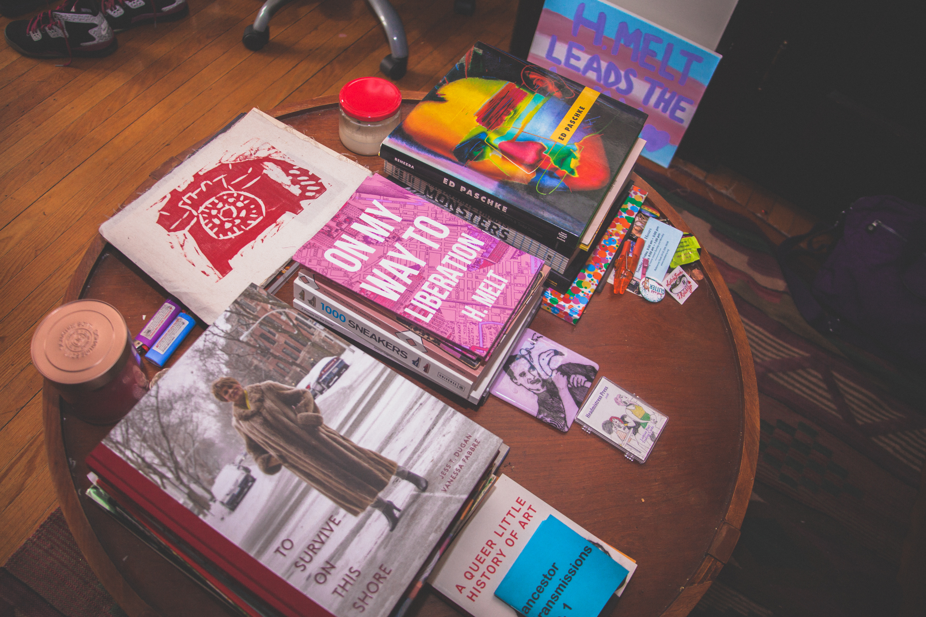 Image: Stacks of books and zines sit on a round table in H. Melt's apartment. These include "To Survive on This Shore," "A Queer Little History of Art," "ancestor transmissions 1", and H. Melt's book "On My Way to Liberation." Photo by Ally Almore.