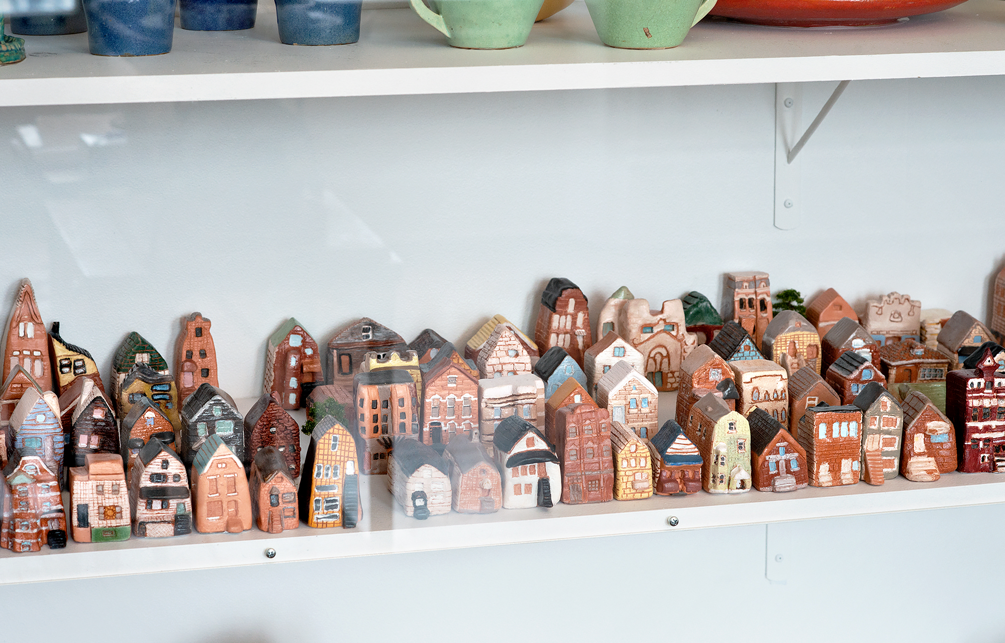 Image: Detail view of ceramic houses and stores made by Nicole Marroquin’s students at Benito Juarez Community Academy High School, as seen in a display case at Hull House. The small ceramics reflect a range of different building styles, from brick to colorful siding, and single-family homes to apartment complexes. They are arranged in dense grids similar to the layout of Chicago neighborhoods. Photo by Greg Ruffing.