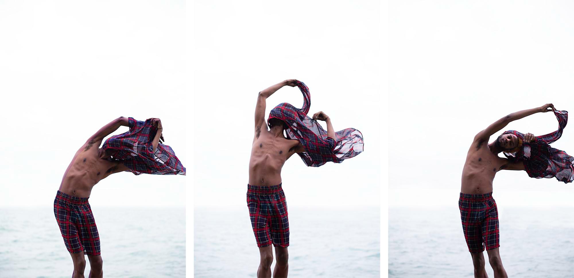 Image: A triptych of Wallace standing in front of a body of water, taking of a sheer plaid shirt. Each image shows Wallace with the shirt over his head, in different postures, and points of disrobing as the shirt waves in the wind. Photo by Chelsea Ross