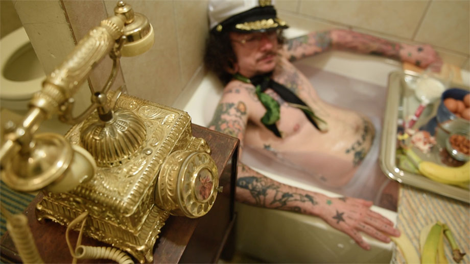 Image: Film still from "Sextra Curricular Activity", featuring actor Jack W. Cooper. In this scene, Jack’s character receives a prank phone call while taking a hot soak in the tub and enjoying some light snacks. Photo courtesy of Heather Raquel Phillips.