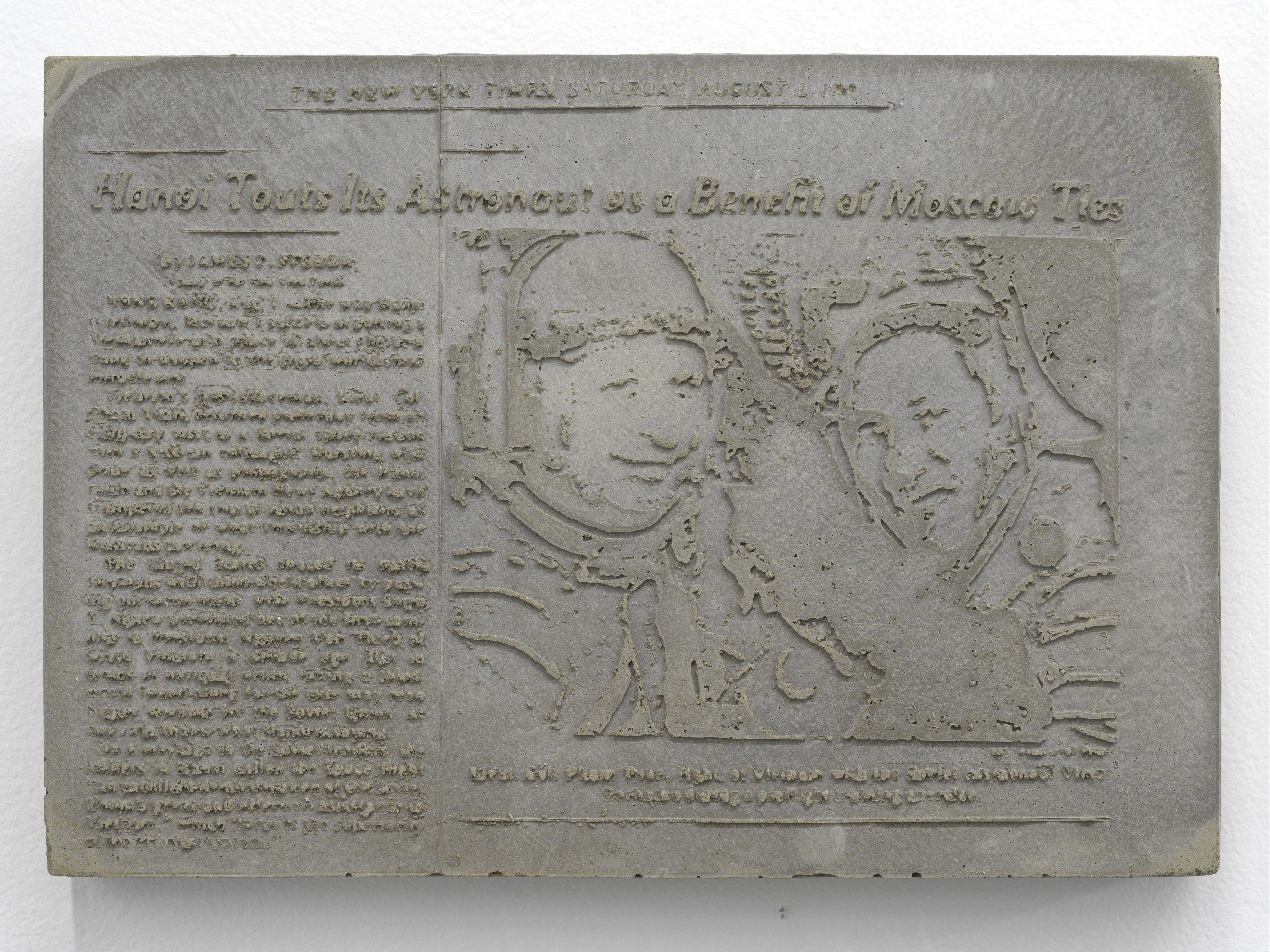 Image: Photo of a newspaper article from the New York Times cast in concrete. The headline reads, “Hanoi touts its astronaut as a benefit of Moscow ties,” The article shows an image of two astronauts wearing space suits and smiling. Image courtesy of the artist.