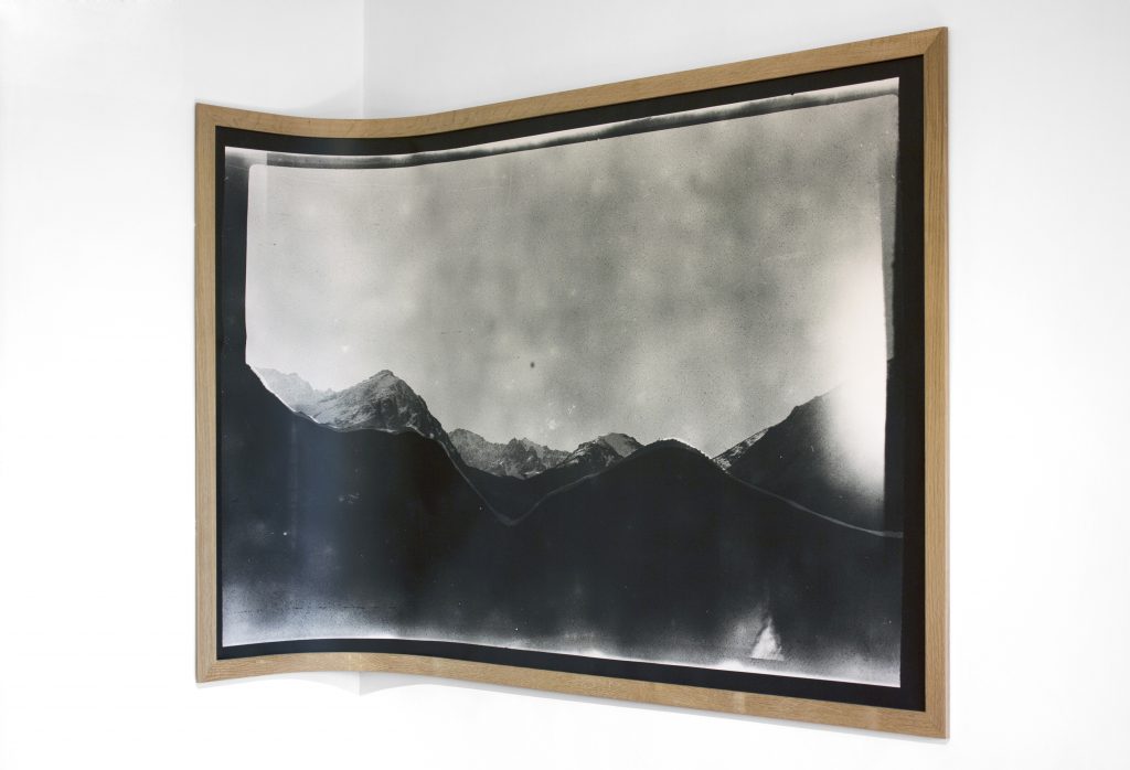 Image: Andre Keichian, 'Salt in the I' (detail), 2019. A large black and white landscape photograph mounted on wood curves against the corner of the room, as part of the exhibition installation at table. Photo by Kim Becker. Image courtesy of Kyle Bellucci Johanson.
