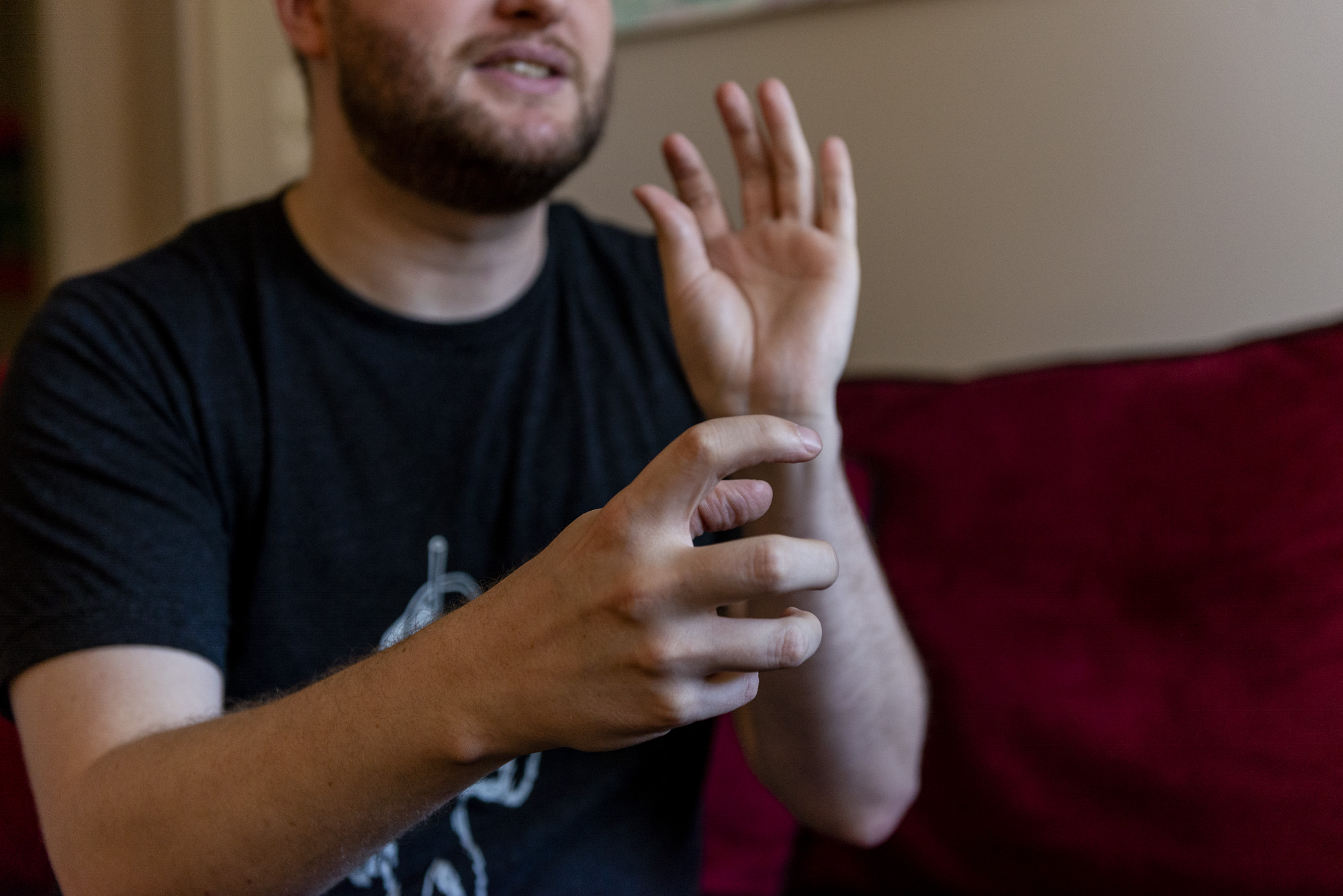 Image: The image is focused on the artists hands. The hand in focus and closest to the viewer is grasping something while the left hand is in motion towards the artists face. Photo by Ryan Edmund Thiel.