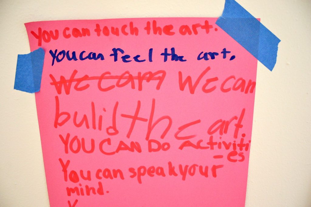 Image: A sign at Pink House, St. Louis. The sign is bright pink and reads, in red and blue marker, in a child’s handwriting: “You can touch the art. You can feel the art. We cam We can build the art. You can do activities. You can speak your mind.” The sign is attached to a white surface using blue tape. Photo by Patrick Fuller. Courtesy of the artist.