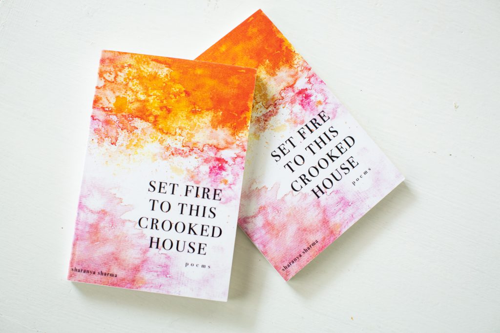 Image: Two copies of Sharanya Sharma’s MFA thesis, a poetry collection entitled “Set Fire to This Crooked House.” The thesis is bound with a colorful cover, on which orange and pink watercolors fade into each other and into white. The title appears in all capital letters and the words “poems” and “sharanya sharma” in all lower-case. Photo by Kristie Kahns Photography.