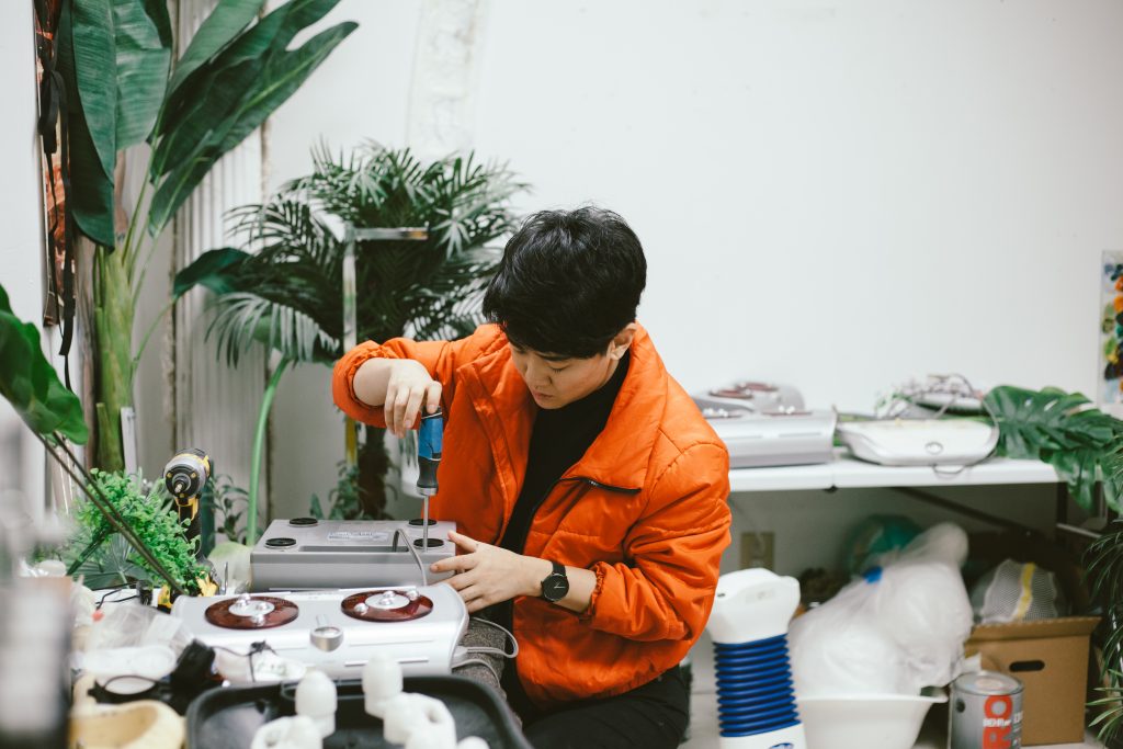 Rachel Youn in their studio hacking a massager with a screwdriver. Photo by Krista Valdez.