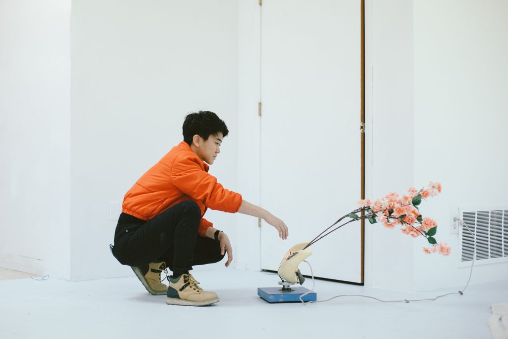 Rachel Youn with a work in progress in their studio. The work is made of massagers, artificial plants, and speaker cabinets. Photo by Krista Valdez. 