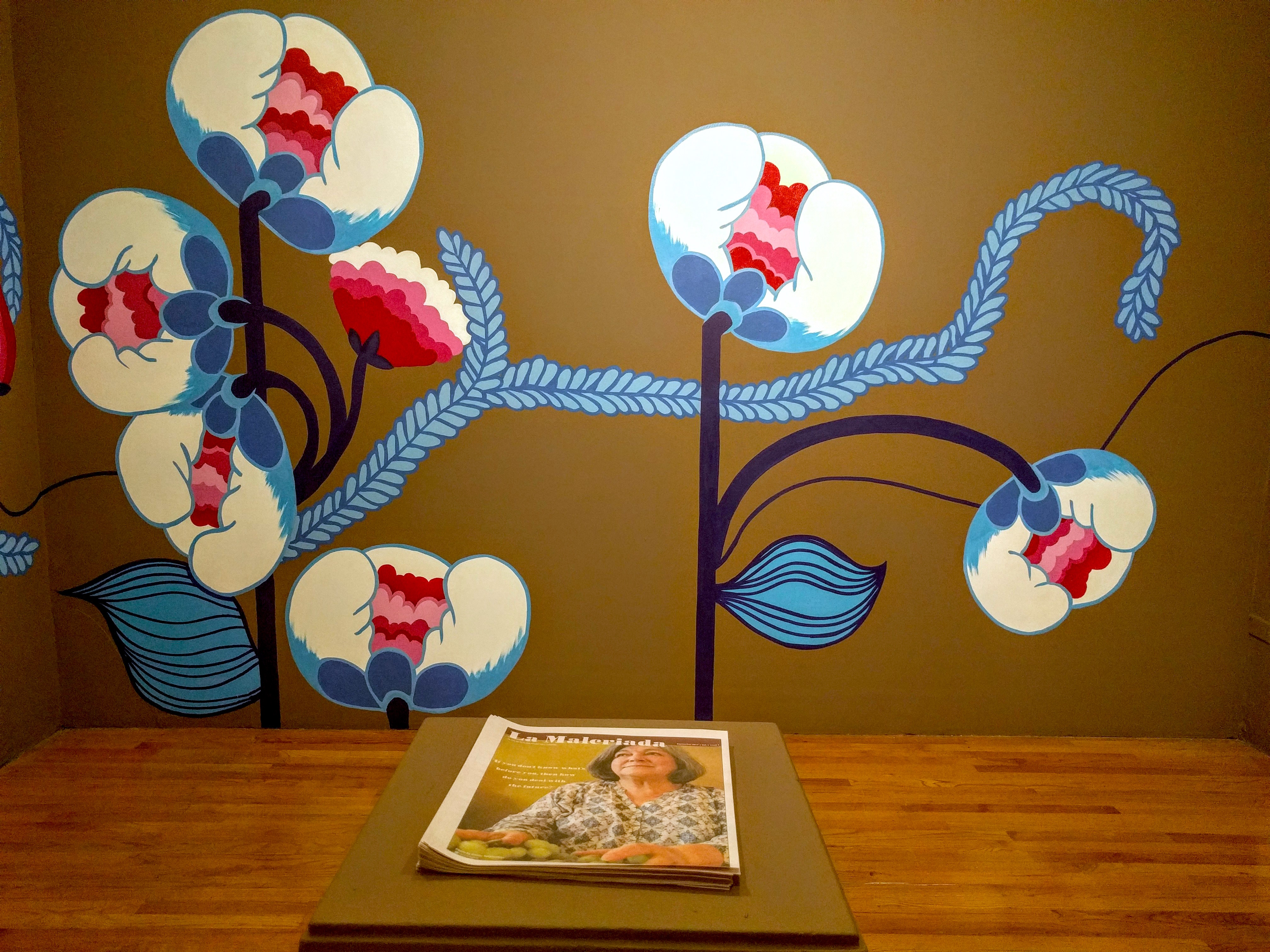 Mural of white, blue and pink flowers on a brown wall with a newsletter on a pedestal.