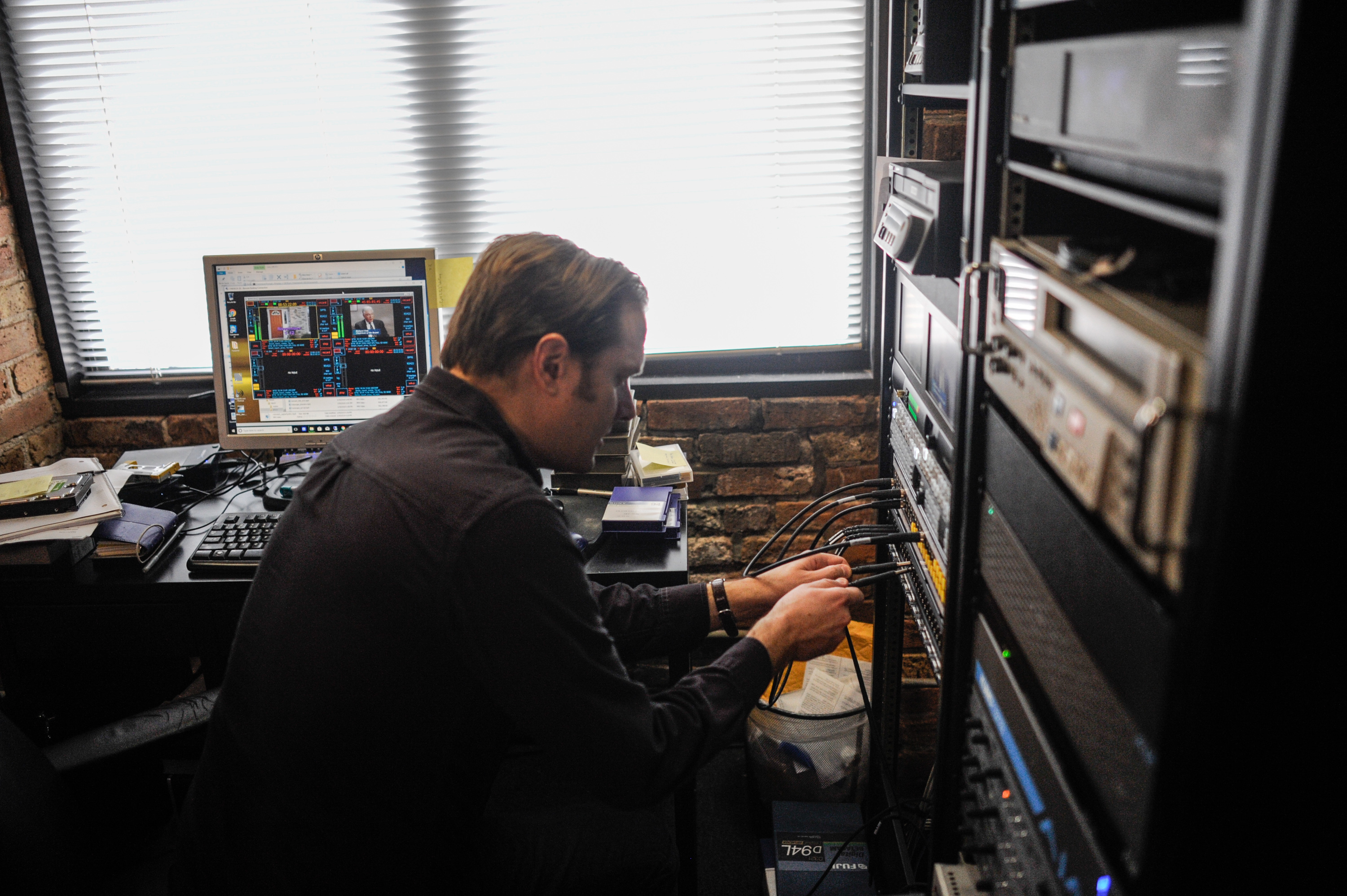 Archivist Dan Erdma plugs a wire into equipment at Media Burn. He is surrounded by various equipment used for digitizing and playing different video formats. Photo by William Camargo.
