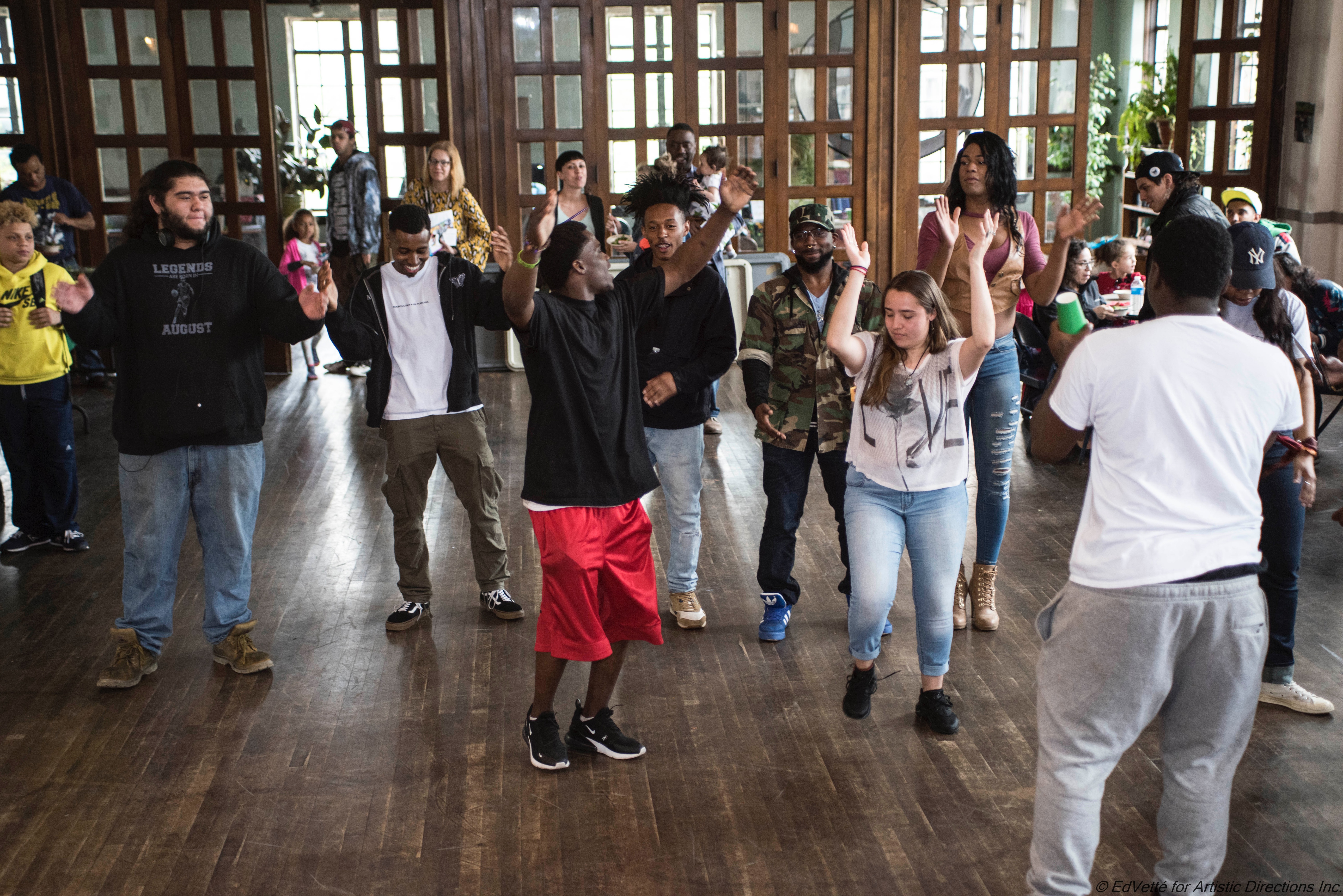 People in attendance at open community event stand with arms raised participating in a community dance.