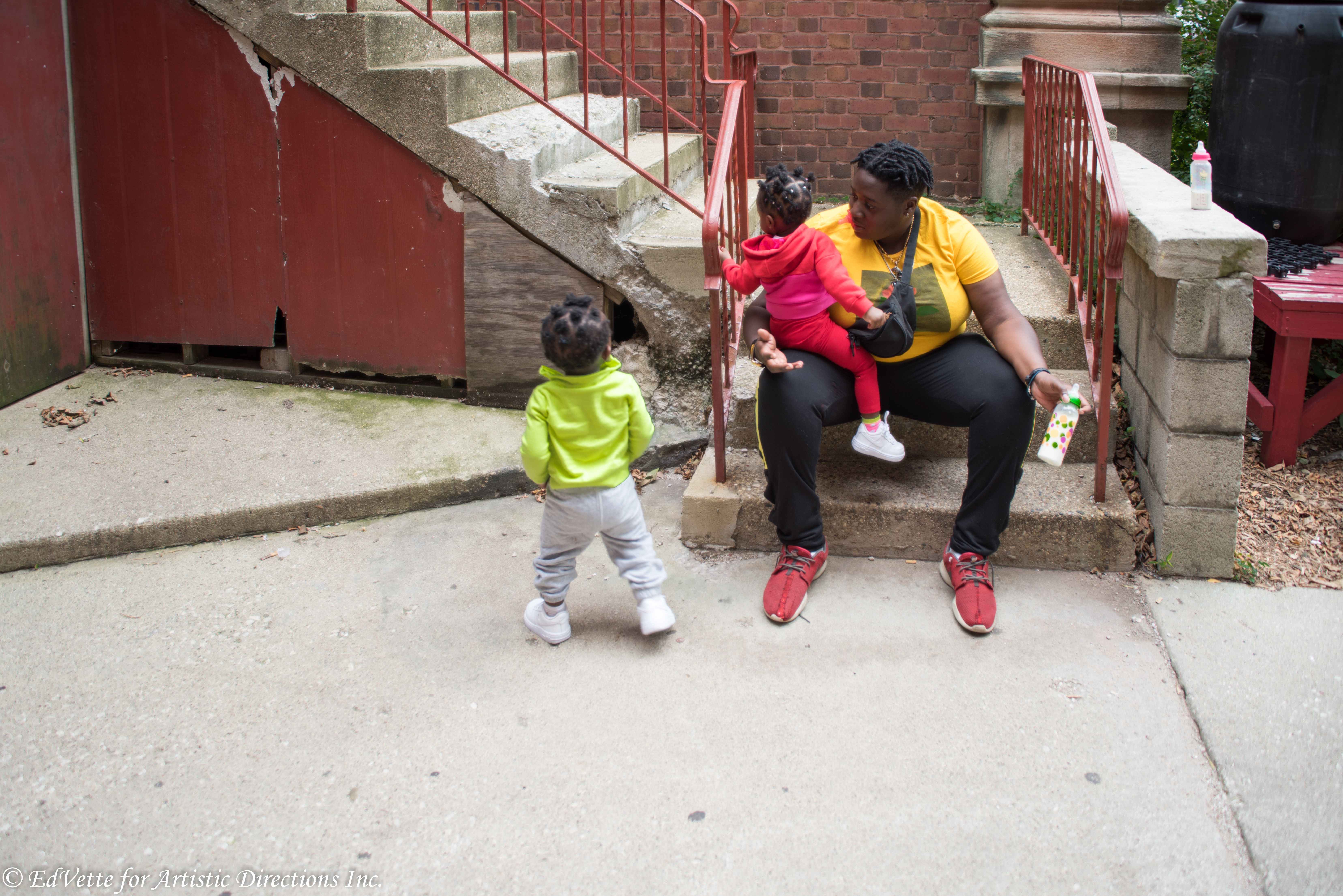 IMAGE: AnnMarie Brown sits on a stairwell outside of United Church of Rogers Park with a child seated on her lap and another standing a short distance away.