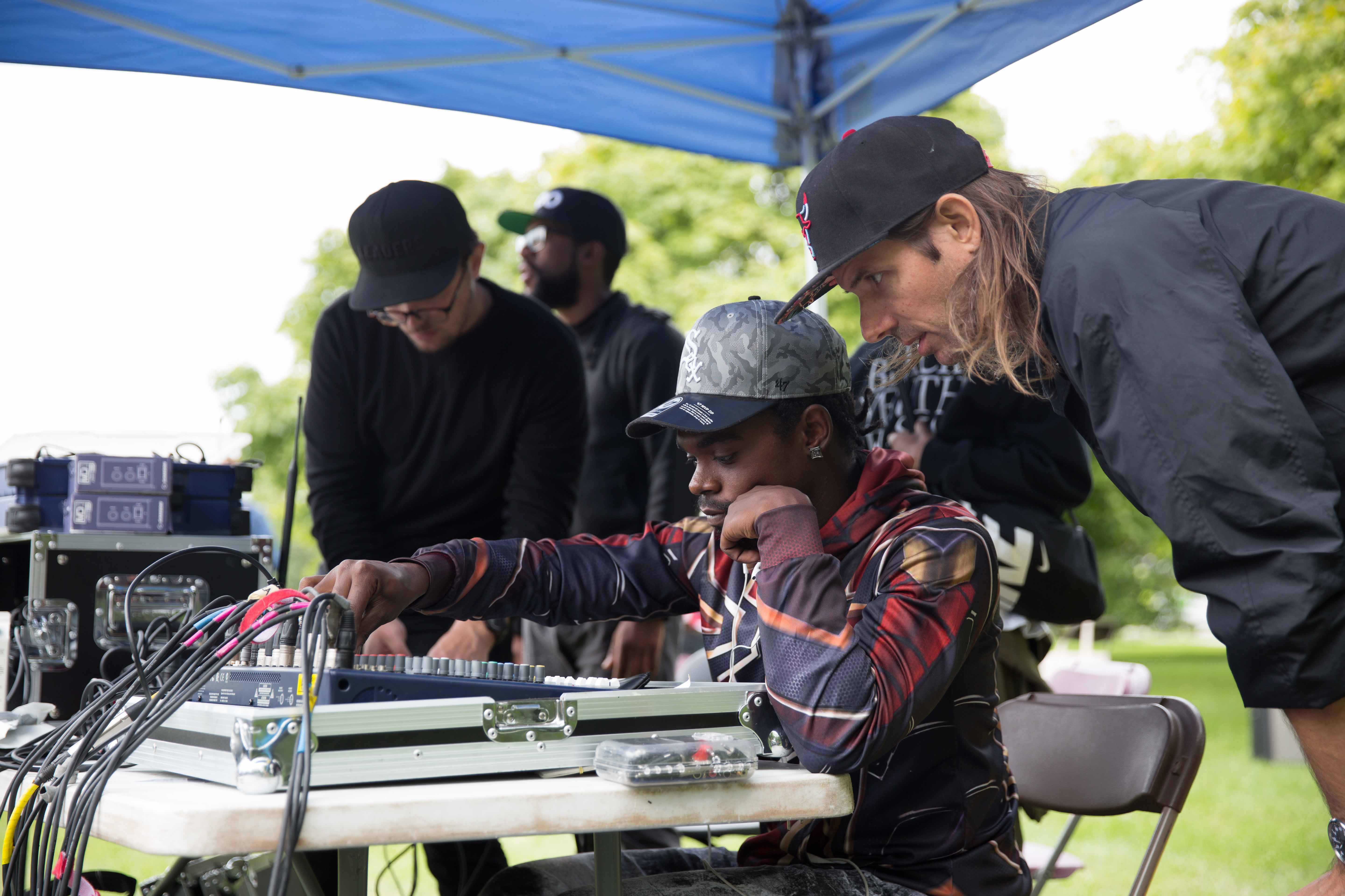 Featured image: Ryan Keesling leans over the shoulder of Walter, a Free Write Sound and Vision technician, as they both look at audio mixer that sits on a table in front of them. They are outside, under a blue tent, where Sound and Vision is mixing sound for the FEAST festival that took place September 8. Photo by Chelsea Ross