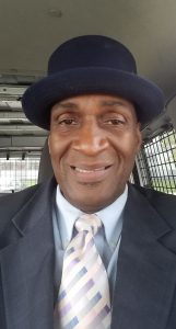 Image: A portrait photograph of Danny Franklin. He is smiling into the camera and wearing a suit and tie and a bowler cap. Photo courtesy of Danny Franklin.