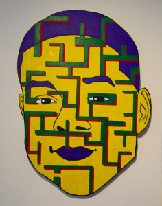 Image: Self-Portrait by Eric Blackmon, from the recent Prison + Neighborhood Art Project exhibition entitled Weight of Rage. The piece is predominantly yellow with green and red lines going across the face. The lips, eyebrows, and hair are purple. Image courtesy of the artist.