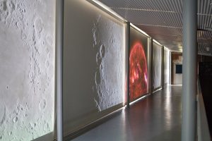 Image: Installation view of "Dark Matter: Celestial Objects as Messengers of Love in These Troubled Times" by Folayemi Wilson. Catwalk with rotating NASA videos of the sun and moon. Photo by Michael Sullivan.