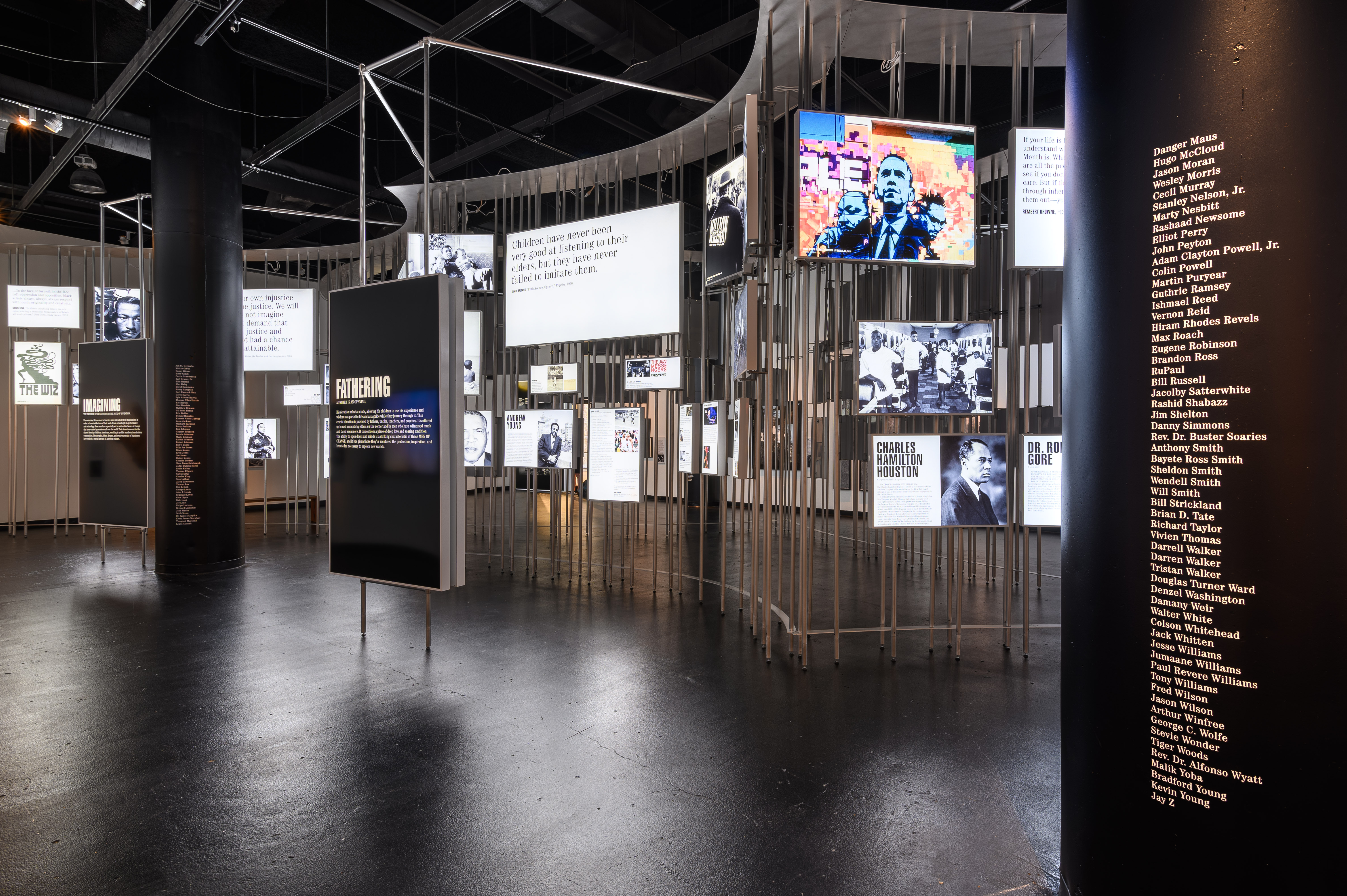 Image: Installation view of Men of Change. The installation made of metal poles is in the middle of the room. Light boxes of various sizes featuring photos and text are hung on the metal poles. Two large displays are in front of the poles: one says IMAGINING and the other says FATHERING. Two large, black architectural columns, one on the right of the image and one on the left of the image feature the names of men of color in alphabetical order. Photo by Phil Armstrong. Photo courtesy of the Smithsonian Institution Traveling Exhibition Service.