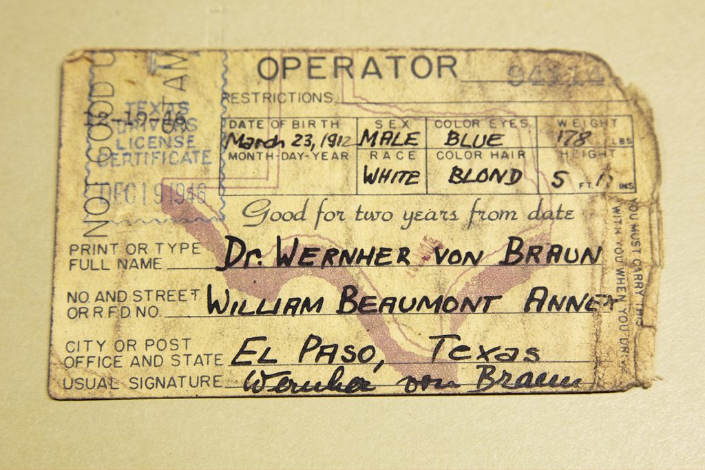 Image: Dr. von Braun's First US Driver's License Certificate, 1946/2019 by Barbara Diener. The image is of a yellowish-beige driver's license from 1946 sitting on a similarly colored surface. Image courtesy of the artist.