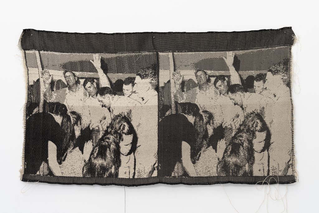 Image: Revival II, 2016 by Cass Davis. Jacquard woven cloth, 13 x 28". The cloth has two near identical images of a revival scene in black and white. The scenes show a crowd of people with their hands in the air. The piece hangs on a white wall. Image courtesy of the artist. Photo by Nick Albertson.