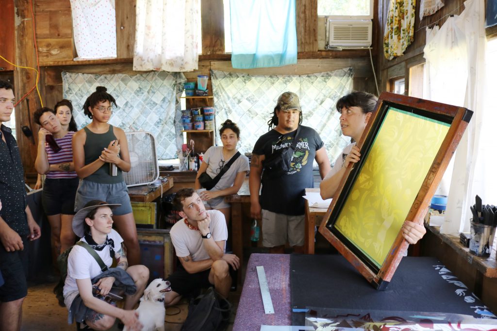 Image: As part of ACRE’s residency program, artists are sitting and standing while watching a screen-printing demonstration. Photo by Zachary Hutchinson, courtesy of ACRE. 