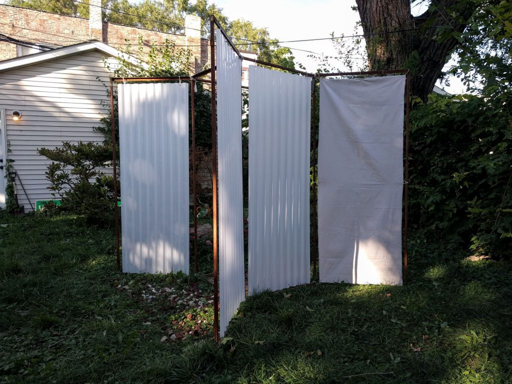 Image: "Avesso" by Cecilia and Marina Resende Santos, on view at The Franklin in Garfield Park from September 30, 2020 to the end of the year. The octagon metal frame that was used for other Open Sheds installations are installed in a way that creates an open 'X' shape. White, hanging material create walls in the structure. Photo by Cecilia and Cecilia Resende Santos