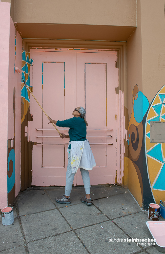 Image: Dorian working on the formerly known South Shore Bank in 2020. They stand in front of a pink wall while painting the side of a building. Photo by Sandra Steinbrecher.