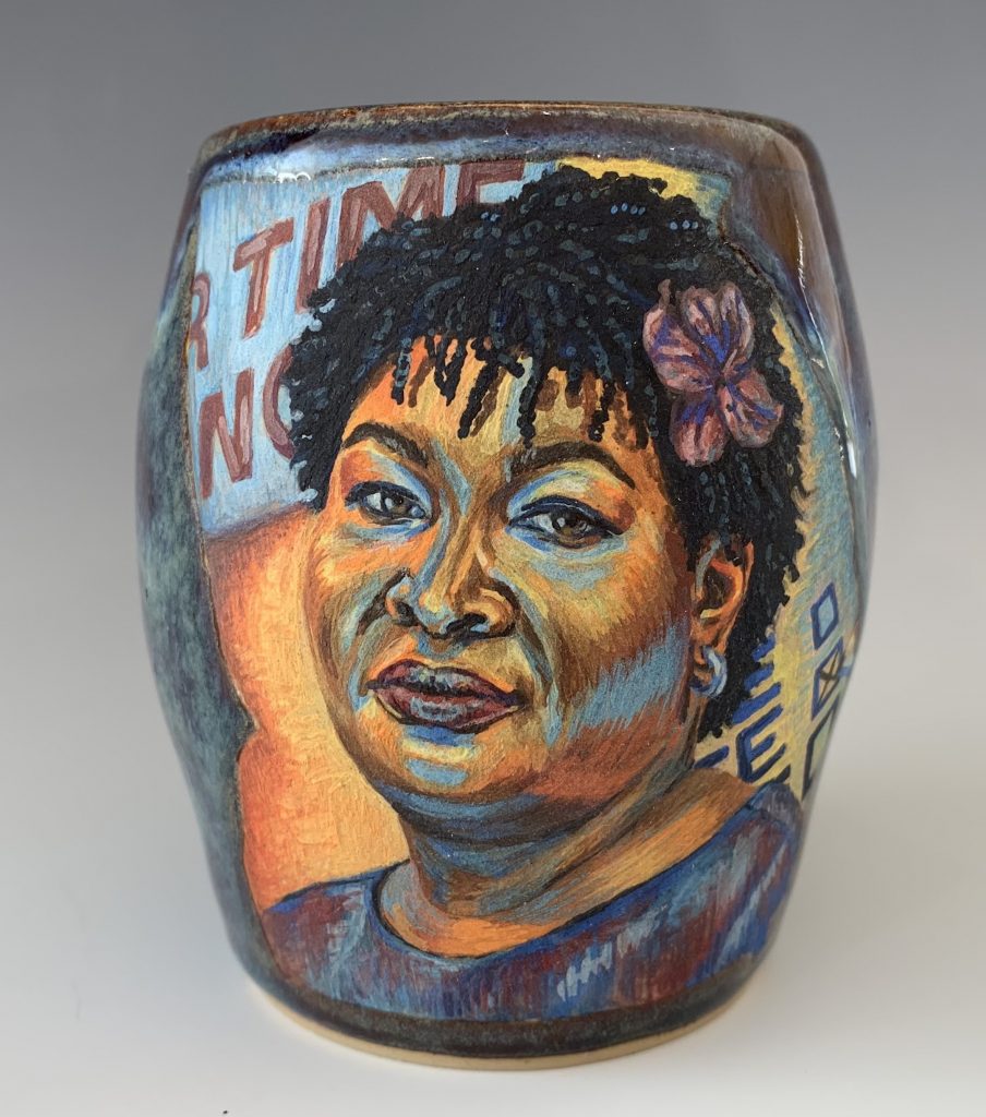 Image: Cristal Sabbath, Stacey Abrams, 2021, stoneware with underglaze watercolors and cone 6 glaze. A vessel with a vibrant portrait of Stacey Abrams. Photo by  Jonathan Castillo. Courtesy of Glass Curtain Gallery.