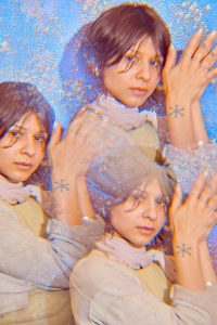 Image: Marissa Macias faces the camera with her hands together towards her head. Three images of Marissa are arranged like a kaleidoscope on a silvery-blue background. Photo by Sarah Joyce.