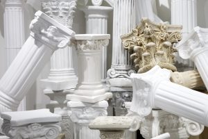 Image: Kelly Kristin Jones, "Orders of Empire," 2020 - ongoing. Plaster, wood, concrete, fiberglass composite, polyethylene, resin. The installation is a pile of plastic, white, faux columns in the corner of 062 Gallery. Image courtesy of the artist.