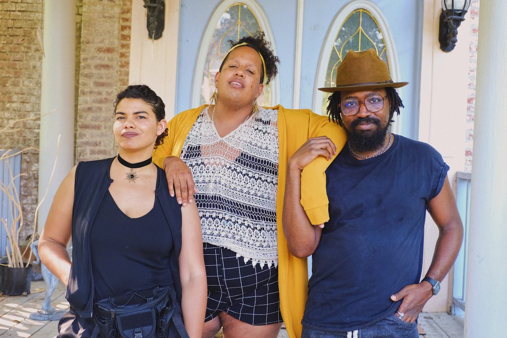 Image: Brenda Pagan, Alexander Martin, and Erick Minnis stand side-by-side, arms draped over one another or interlocked, in front of double doors, looking directly into the camera with the sun shining around them. Photo by Erick Minnis.