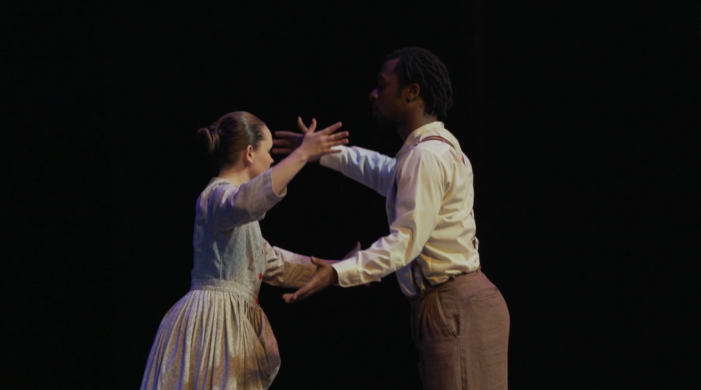 Image: A film still from Let Our Loss Be Heard. Actress Hannah Duvall as Mary Garner
and actor Marcellus Howie as Robert Garner reach out to embrace one another. They are playing characters that are father and daughter. The background is completely dark. Courtesy of Mourning the Creation of Racial Categories Project.