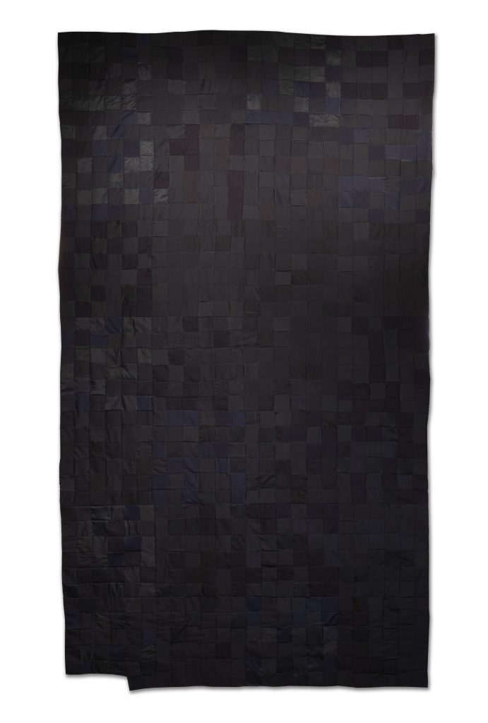Image: Carolyn Drake, "The number of Americans killed by police officers in 2019," 2020. Police uniforms made from polyester, nylon, wool, and cotton. A vertical quilt composed of 1,004 black fabric squares hangs on the wall like a tapestry. Courtesy of the artist.
