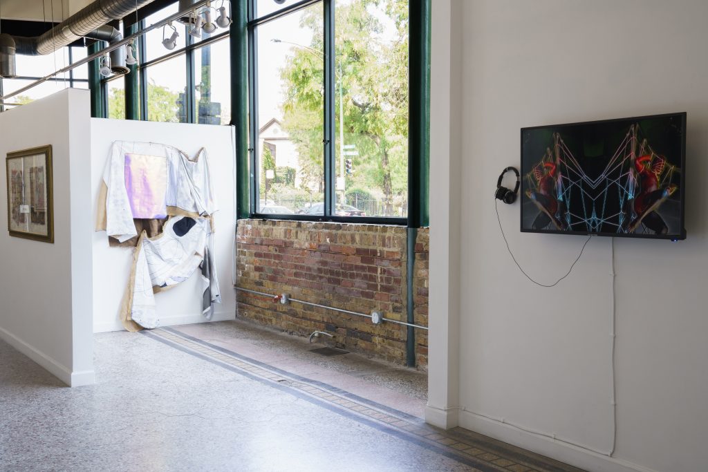 Image: A view of "Dreamscapes: Imaginings of a Black Pastoral" at Roots and Culture. On the right side is a video piece installed on a screen on the wall. On the left are several pieces on view, one being a framed collage and the other being a large textile piece. Photo by Colectivo Multipolar.