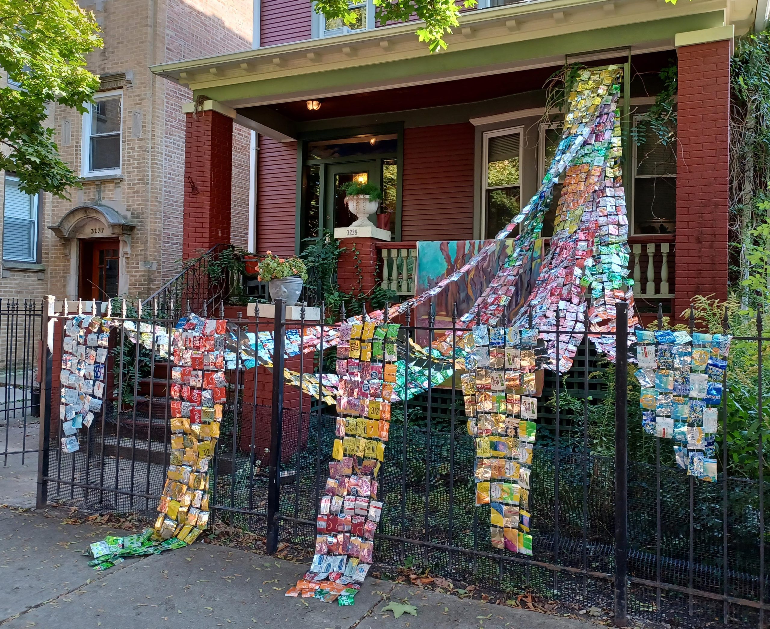 Featured image: Laurie LeBreton, “Collective Effervescence,” 2021. 750 aluminum cans and 350 feet of waxed linen twine. Colorful ribbons patterned from cans are draped from the front porch and over the fence. Courtesy of Kitty Goldbert.