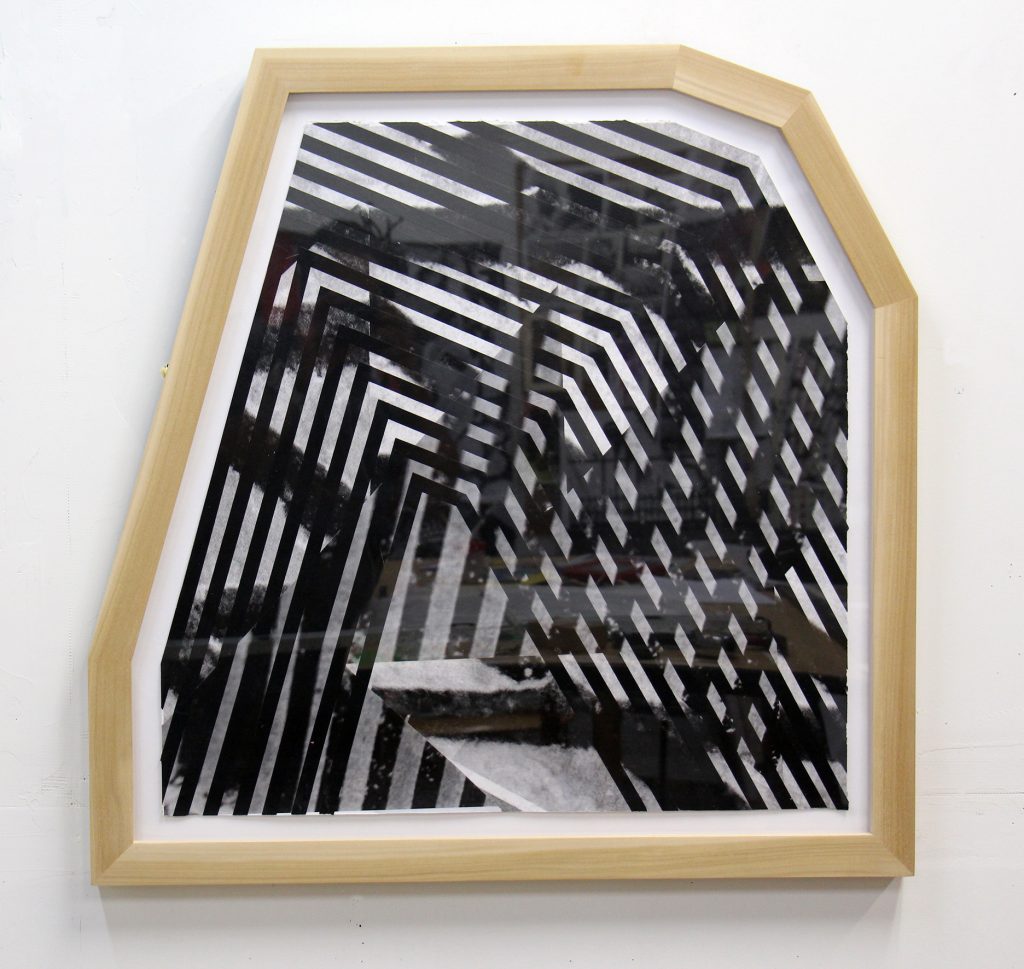 Image: Esau McGhee, Razed Landscape #3, 2014. A framed, geometric piece of art that is made of of criss-crossing black lines on a white surface. The piece hangs on a white wall. Image courtesy of the artist.