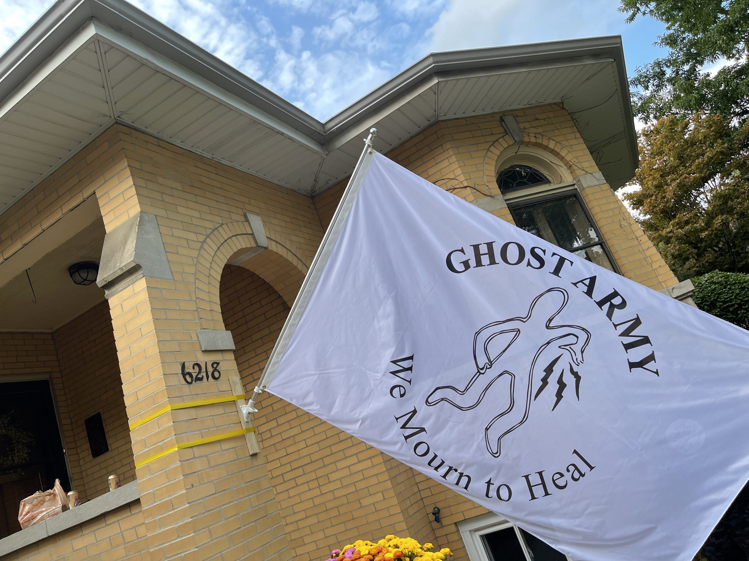 Featured image: Michael Workman, “Ghost Army” flag 2021. A white flag depicting an outline of a figure with the words “GHOST ARMY/We Mourn to Heal” hangs from the front entryway. Courtesy of the artist.