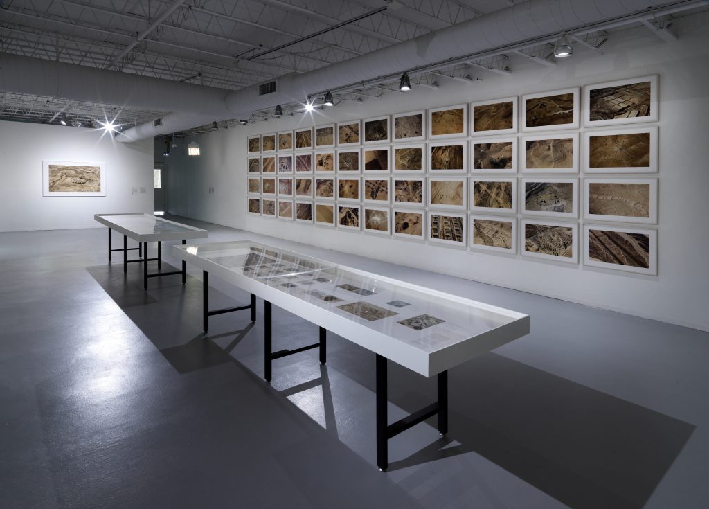 Image: Full installation view of Fazal Sheikh's piece "Desert Bloom" on display at Toward Common Cause: Art, Social Change, and the MacArthur Fellows Program at 40 at Hyde Park Art Center. The piece contains 48 inkjet prints of aerial photographs that were taken in 2011. Image courtesy of Hyde Park Art Center