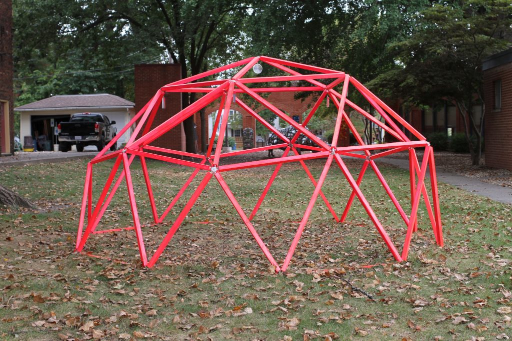 Image: Erin Washington, afterglow of radiation at 801 N 5th Street, Springfield IL. A dome-like, red structure comprised of many triangle shapes sits on the grass. Photo by Jeff Robinson.